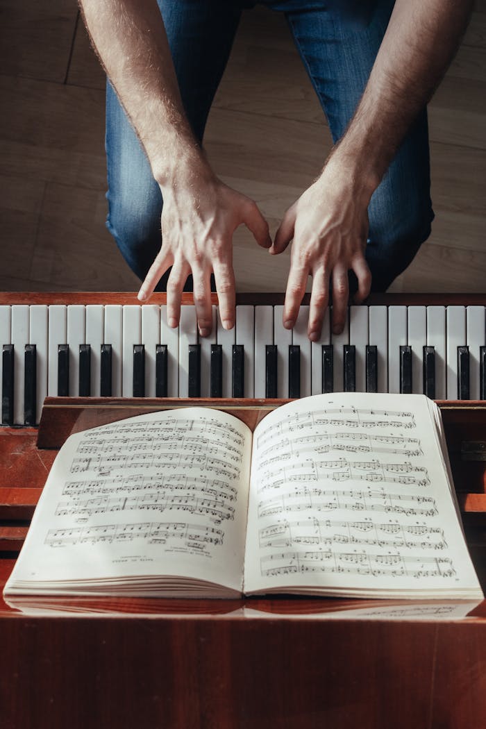 Top view of crop unrecognizable male musician plating piano with music paper on stand during rehearsal